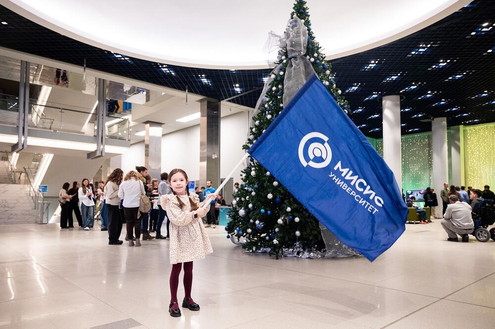 Маленькая девочка, посетитель Дня открытых дверей, держит большой флаг НИТУ МИСИС